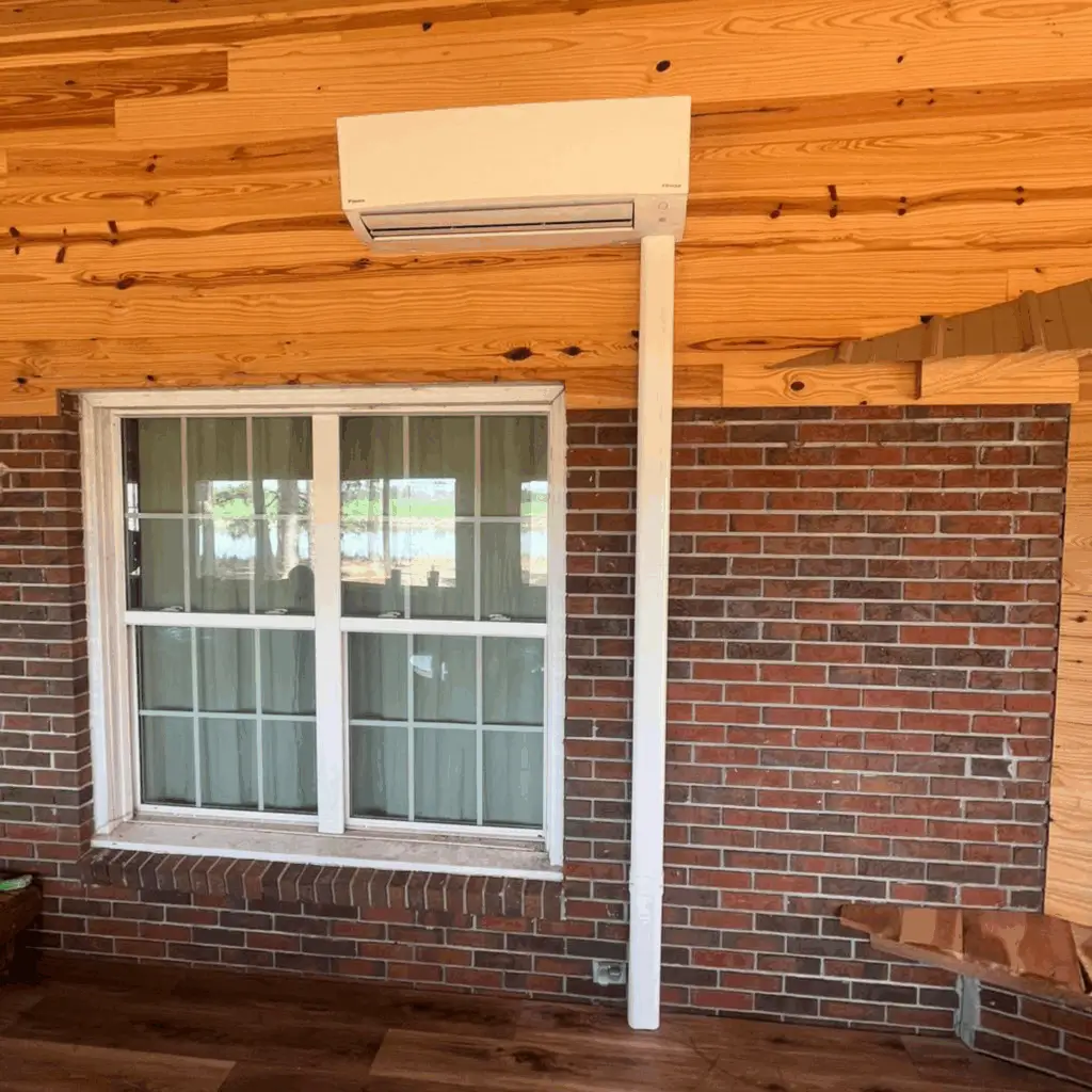 Air conditioner installed on a brick wall below a window.