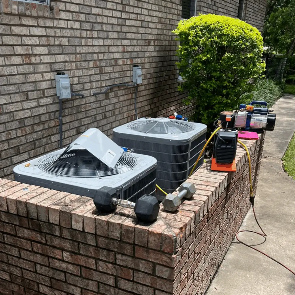 Two air conditioning units on a brick platform beside a house.